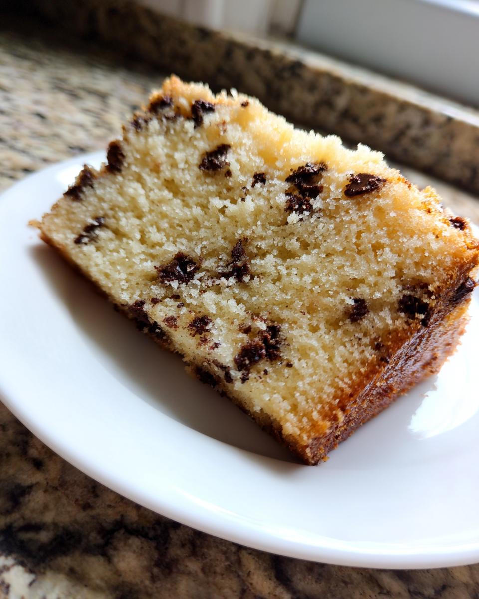 Close-up of a moist slice of vanilla chocolate chip cake served on a white plate.