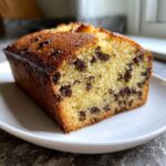 Close-up of a moist slice of vanilla chocolate chip cake showing dark chocolate chips throughout the yellow crumb.