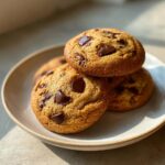 A stack of four golden brown vanilla pudding chocolate chip cookies loaded with melted chocolate chunks on a light plate.