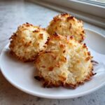Three perfectly baked vegan coconut macaroons with toasted edges resting on a white plate.