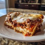 A thick, cheesy slice of lasagna with rich meat sauce and melted mozzarella on a white plate.