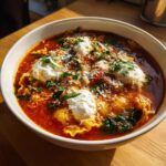 Close-up of a bowl of rich, red lasagna soup topped with dollops of ricotta, grated parmesan, and fresh parsley.