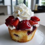 Close-up of a single blueberry muffin strawberry shortcake hybrid topped with fresh strawberries and whipped cream.