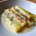 Close-up of perfectly cooked braised leeks with cream and white wine sauce, showing slight char marks.