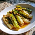 A white bowl filled with tender, glossy french braised leeks sitting in a savory, light brown sauce.