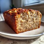 Close-up of a perfectly baked slice of gluten free sugar free banana bread, showing a moist crumb and walnuts on top.