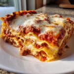 A thick, layered slice of baked lasagna recipe with ricotta cheese, meat sauce, and melted mozzarella on top.