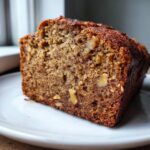 Close-up of a moist slice of sugar free banana bread, showing the crumb texture and visible walnut pieces.