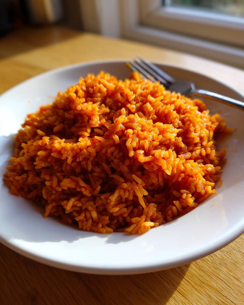 A close-up of a generous serving of vibrant orange smoky jollof rice in a white bowl, ready to eat.