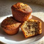 Three golden brown sugar free banana bread muffins stacked on a white plate, one cut open to show the moist interior.