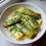 A white bowl filled with tender braised leeks in a creamy sauce, topped generously with fresh chopped chives.